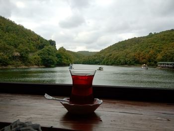 Drinking glass on table by lake against sky