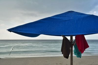 Close-up of umbrella on beach against blue sky
