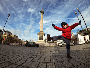 Full length of man with arms raised in city against sky