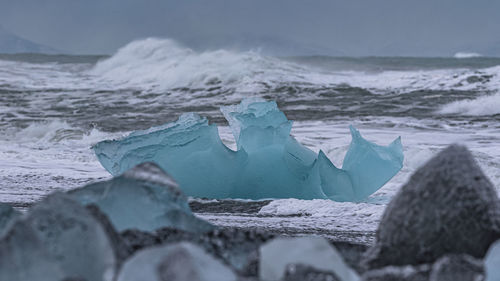 Blue glacier ice on black sand beach with ocean waves in background