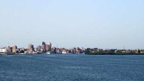 Sea by buildings against clear sky