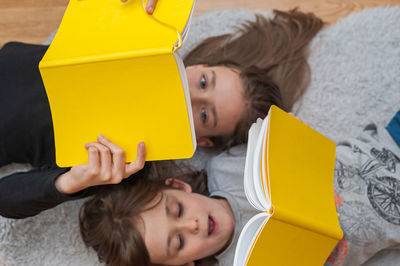 Young girl with her little brother enjoying reading stories together from yellow books