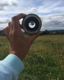 Close-up of man photographing camera on field against sky