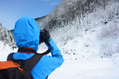 Rear view of backpack woman photographing snowcapped mountain through camera