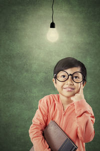 Thoughtful girl wearing eyeglasses while standing against blackboard