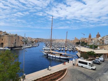 Sailboats moored in harbor by buildings against sky