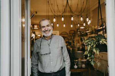Portrait of happy senior male owner standing near door of interior shop
