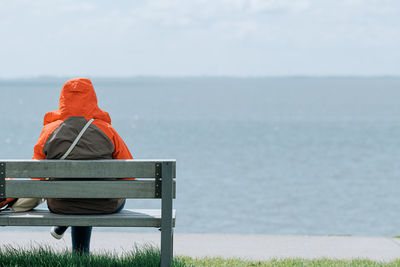 Back view of unrecognizable person sitting on bench at sea