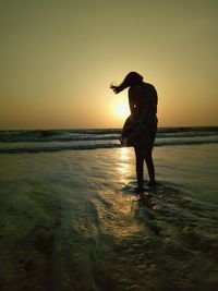 Full length of woman standing in sea against sky during sunset