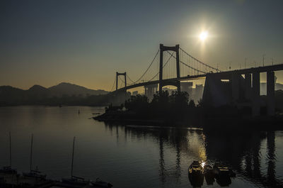 Silhouette bridge over river against sky during sunset