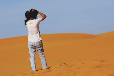 Rear view of man standing on desert against clear sky