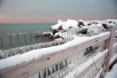 Close-up of snow on railing by sea against sky