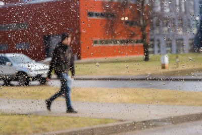 Man walking on footpath seen through wet car window in rainy season
