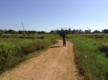 Rear view of woman walking on field against clear sky