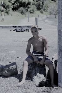 Full length of shirtless man sitting on rock