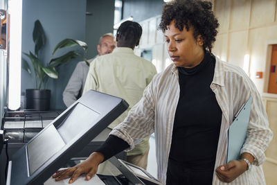 Young businesswoman using photocopier machine with colleagues standing in background