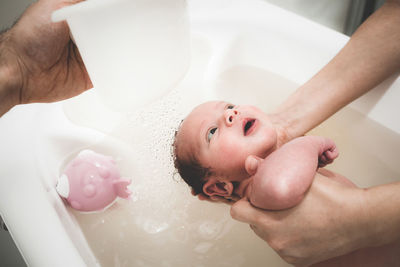 Cropped hands holding baby in bathtub at home