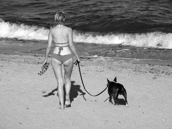 Rear view of sensuous young woman with dog walking on sea shore