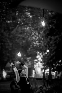 Low angle view of woman holding lit candle against trees