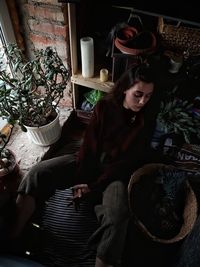 Portrait of young woman sitting on potted plant at home