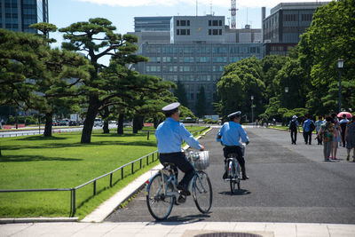 Rear view of people riding bicycle on street in city