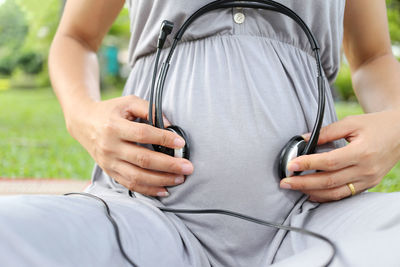 Midsection of pregnant woman holding headphones on belly at yard