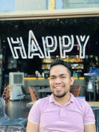 Portrait of happy young man sitting in front of the restaurant.