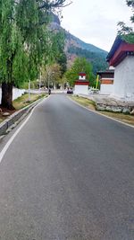 Road amidst trees and buildings against sky