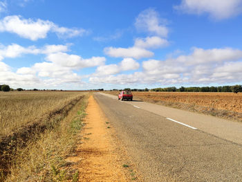 Road passing through agricultural field against sky