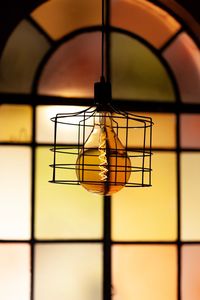 Close-up of illuminated light bulb hanging against window