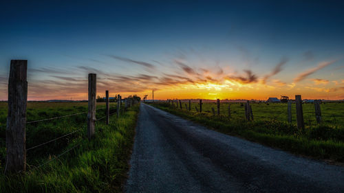 Road amidst field against sky during sunset
