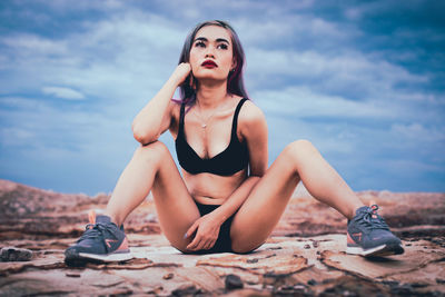 Young woman looking away while sitting against sky