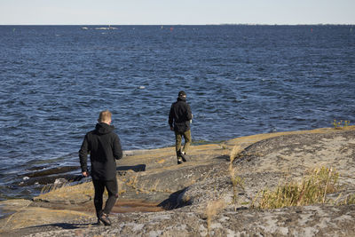 Rear view of men walking at rocky coast