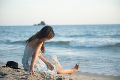 Woman sitting at beach against sky