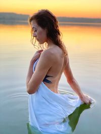 Woman standing by sea against sky during sunset