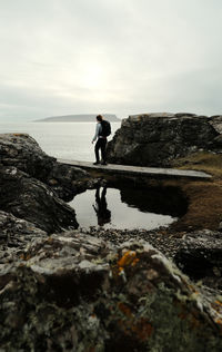 Rear view of man walking on rock by sea against sky