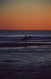 Silhouette person standing on sea against orange sky