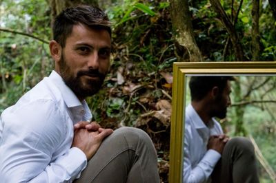 Portrait of young man with reflection on mirror at forest