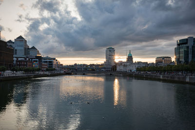 River by buildings against sky during sunset
