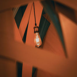 Low angle view of illuminated light bulb hanging on wall