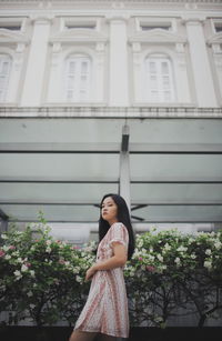 Portrait of young woman standing by plants against building