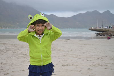 Portrait of cheerful girl standing at beach against mountains