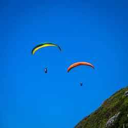 Low angle view of people paragliding against clear blue sky