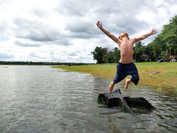 Full length of shirtless man jumping in lake against sky