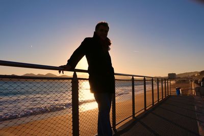 Silhouette person standing by railing against sky during sunset