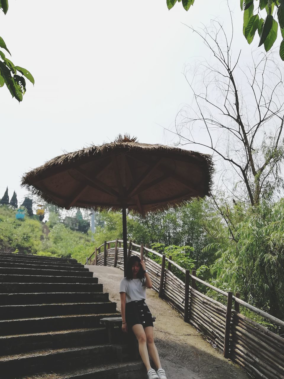 one person, real people, architecture, railing, lifestyles, leisure activity, tree, staircase, women, built structure, full length, umbrella, young women, sky, standing, nature, casual clothing, adult, rear view, steps and staircases, outdoors
