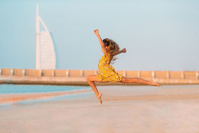 Side view of girl jumping at beach against clear sky