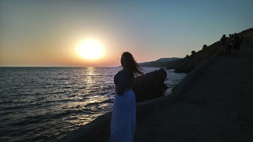 Woman looking at sea against sky during sunset