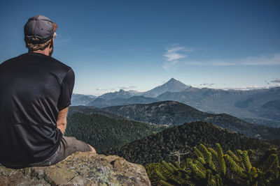 Rear view of man looking at mountains while sitting on rock