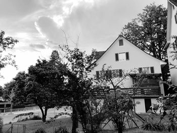 Trees and houses in town against cloudy sky